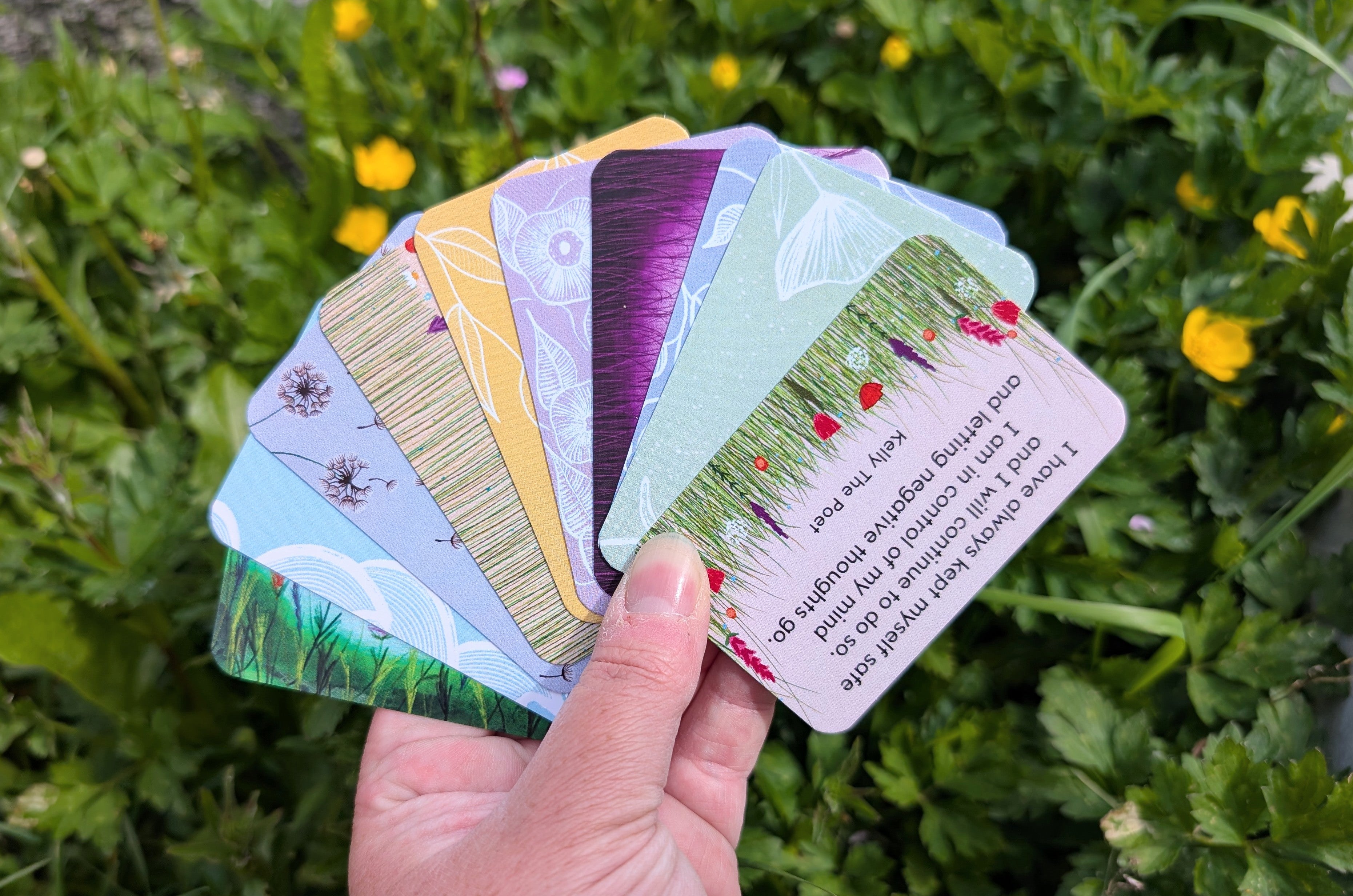 A hand holding a collection of colorful poem cards with nature in the background.