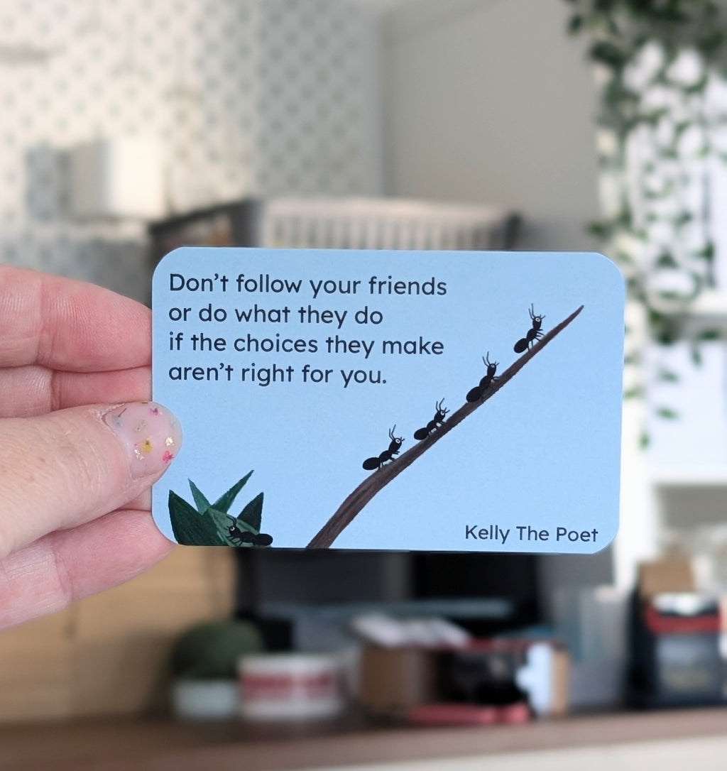 Hand holding a card with a motivational quote by Kelly The Poet against a blurred indoor background.