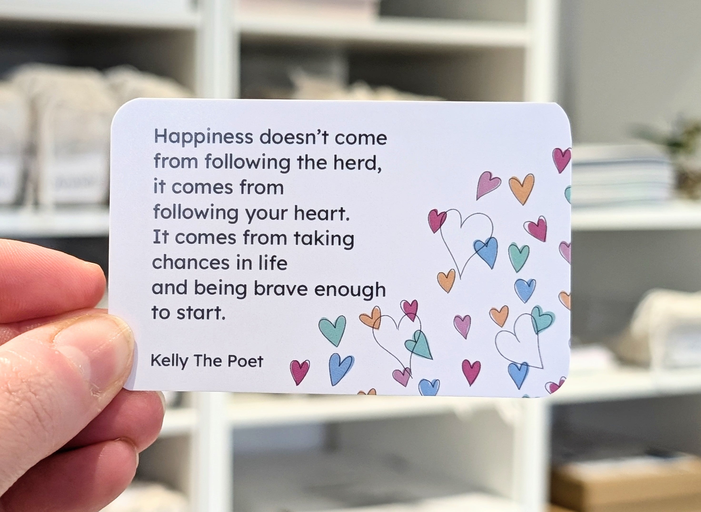 Card with motivational quote and colorful hearts held by a hand, blurred indoor background