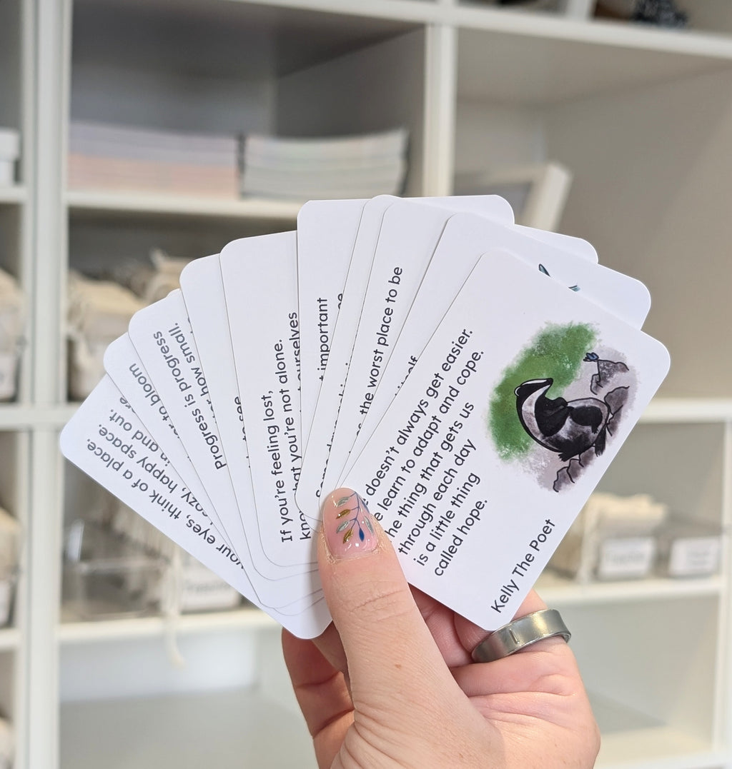 Hand holding a set of cards with text and illustrations, blurred indoor background. Poems to help with grief.