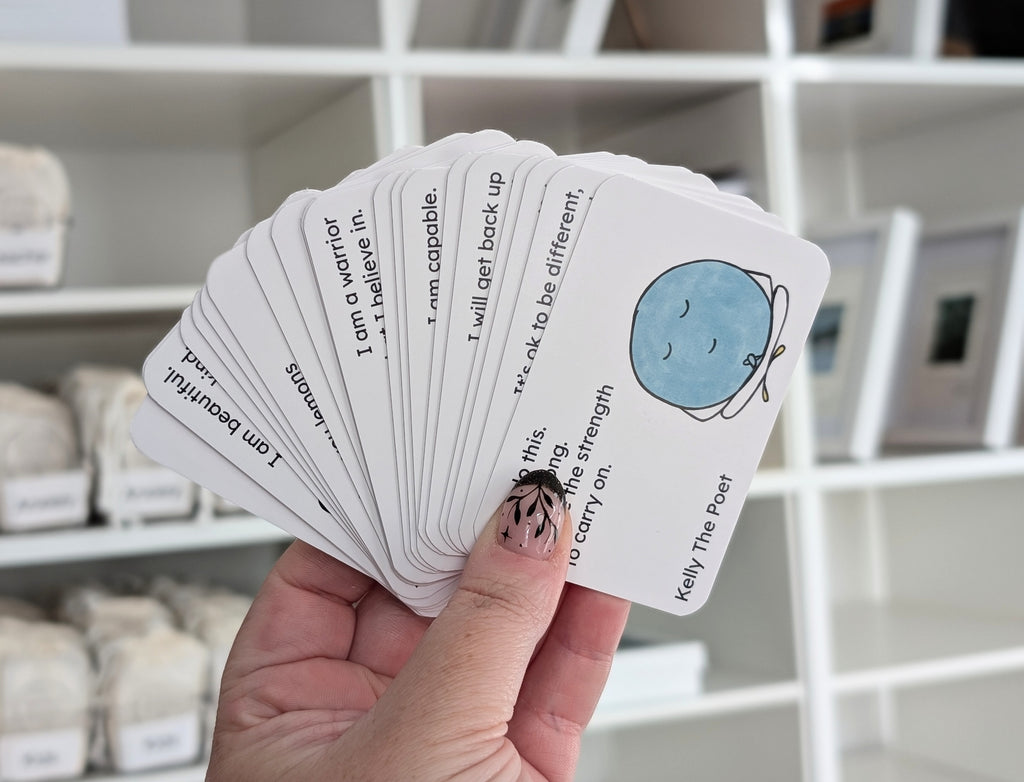 Hand holding a deck of cards with motivational phrases and a blue circle design, with shelves in the background.